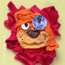 Ein Löwengesicht aus Kleidung und Stoffen, mit einem Erdball als Auge, auf einem hellgrünen Hintergrund.