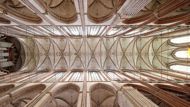 Blick auf die kunstvoll verzierte Decke einer gotischen Kathedrale mit hohen Fenstern und Orgelpfeifen.