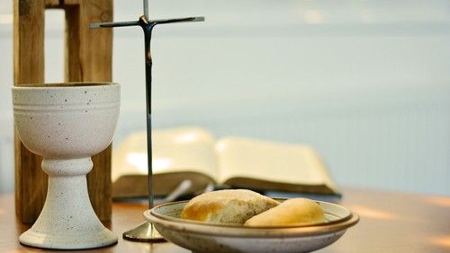 Ein Kelch, ein Kreuz, Brot und eine Bibel auf einem Tisch.