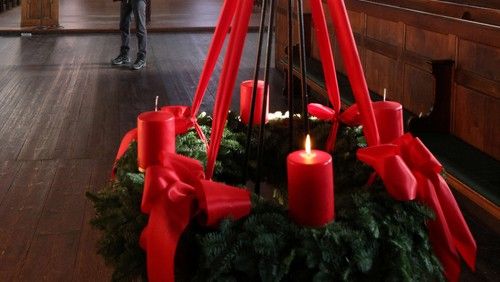 Ein Adventskranz mit roten Kerzen und Schleifen in einer Kirche.