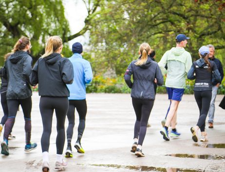 Eine Gruppe von Menschen joggt durch einen Park mit Bäumen im Hintergrund.