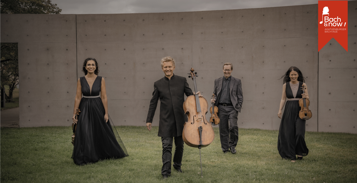 Vier Musiker in eleganter Kleidung mit Instrumenten vor einer Betonwand im Freien.