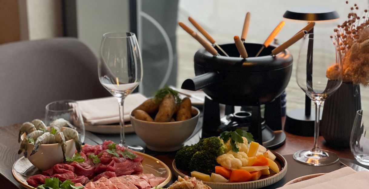 Ein gedeckter Tisch mit Fondue-Set, Fleisch, Gemüse und Dips in einem Restaurant.