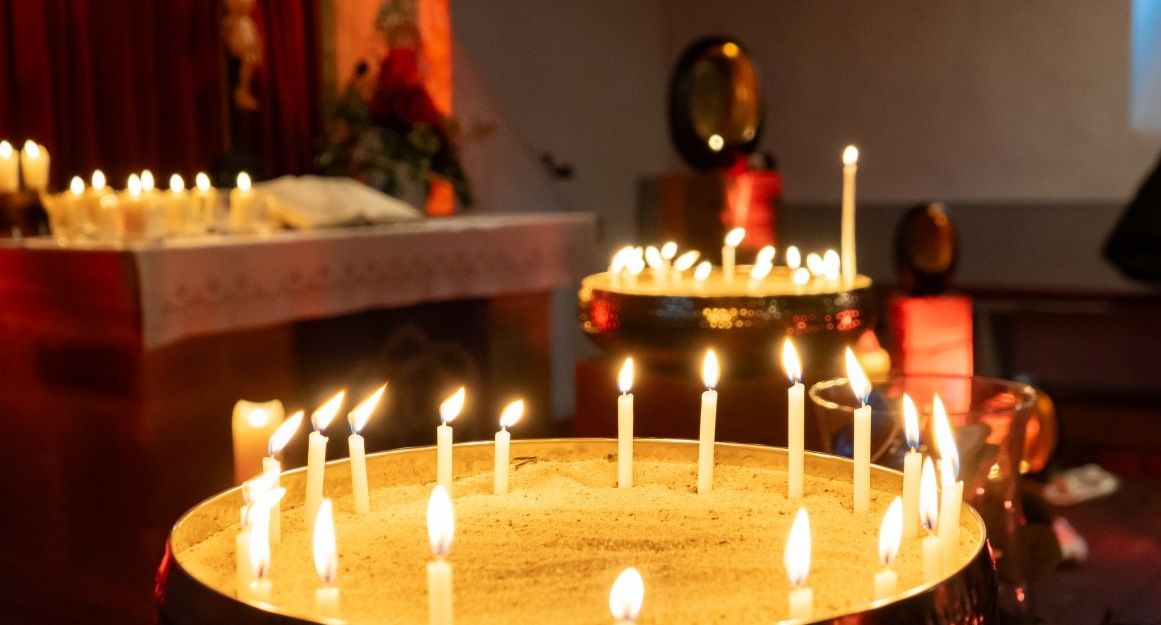 Kerzen in einer Kirche, die auf Sand in Schalen stehen, mit einem Altar im Hintergrund.