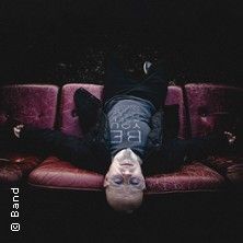 Person liegt auf einem roten Sofa, Arme ausgestreckt, Blick nach oben.