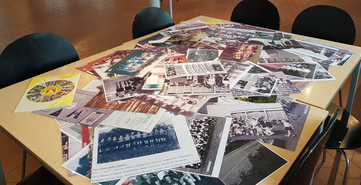 Ein Tisch voller alter Fotos und Dokumente in einem Raum mit Stühlen.