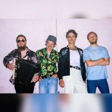 Vier Männer posieren vor einer Wand, einer hält ein Akkordeon.