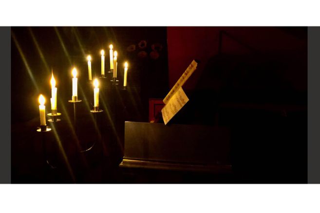 Ein Klavier mit Notenblatt im Kerzenschein, umgeben von mehreren brennenden Kerzen in einem dunklen Raum.