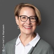 Porträt einer lächelnden Frau mit Brille und kurzem Haar vor grauem Hintergrund.