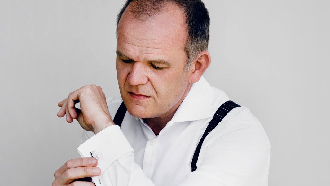 Mann in weißem Hemd mit Hosenträgern schaut auf seine Manschette.