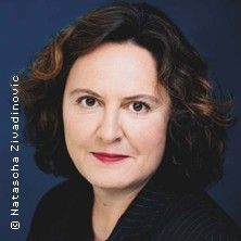 Porträt einer Frau mit dunklen, lockigen Haaren vor einem blauen Hintergrund.