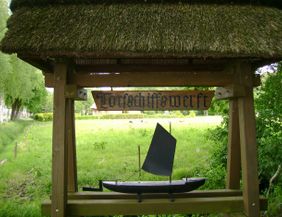 Holzschild mit der Aufschrift 'Torfschiffswerft' und einem Modell eines Torfschiffs darunter.