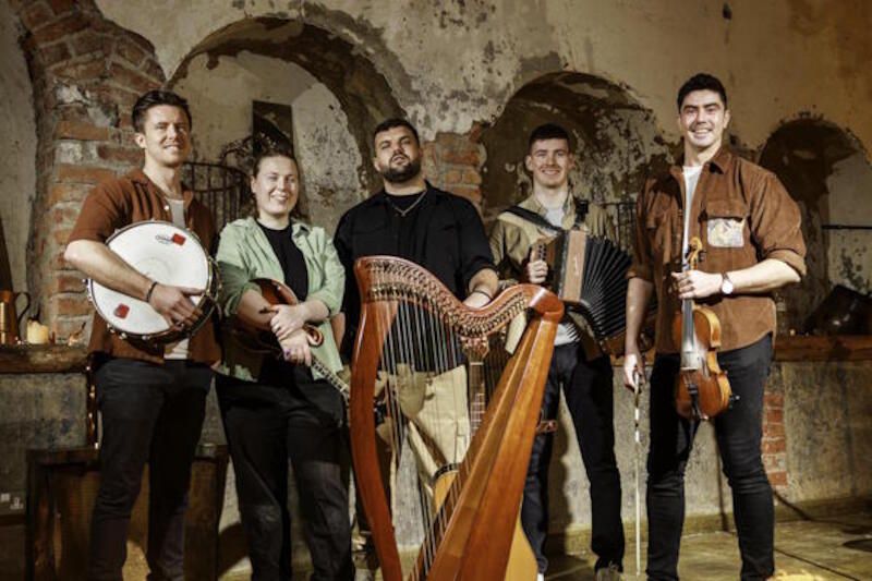 Fünf Musiker mit traditionellen irischen Instrumenten in einem rustikalen Raum.