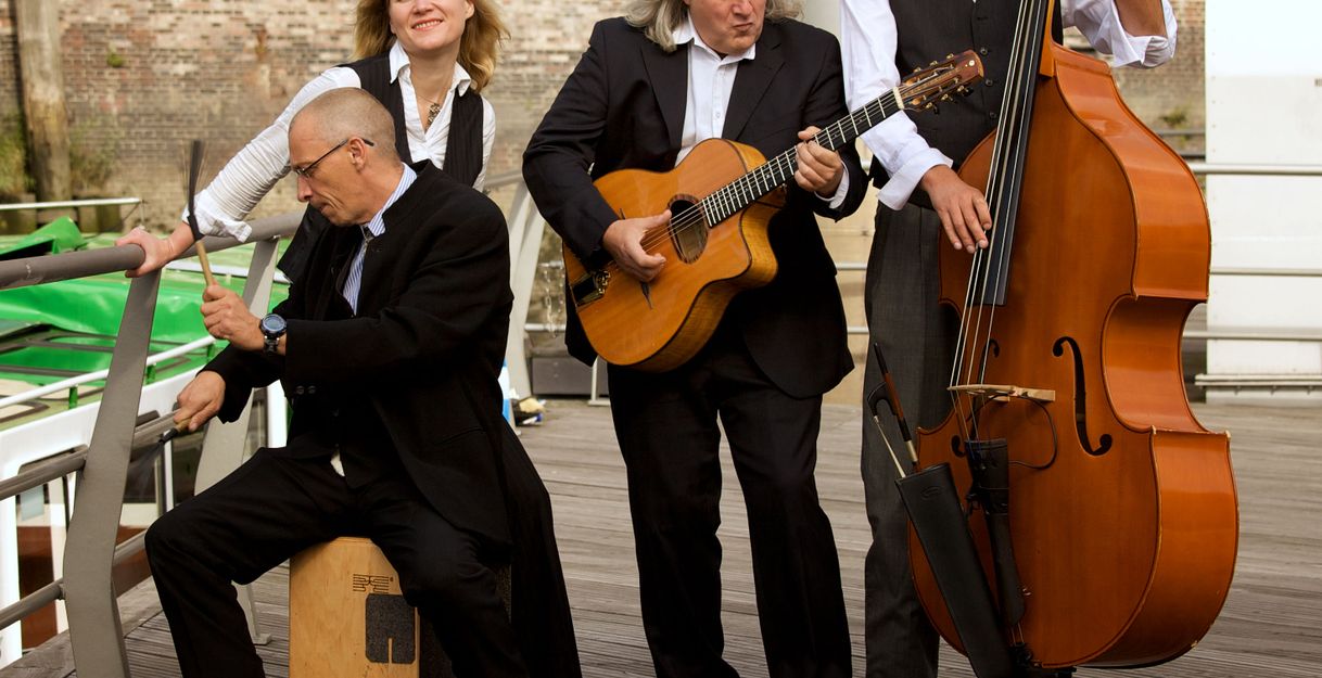 Eine vierköpfige Band spielt auf einem Holzsteg. Ein Mann spielt Cajón, eine Frau lächelt, ein Mann spielt Gitarre und ein anderer Kontrabass.