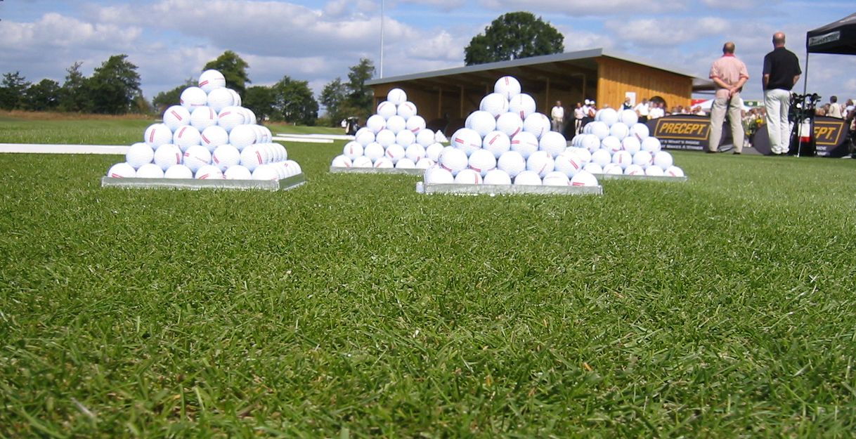 Golfbälle in Pyramidenform auf einer Driving Range mit Personen im Hintergrund.