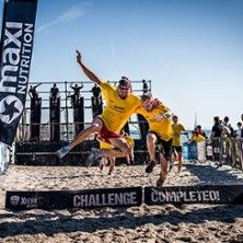 Teilnehmer der Xletix Challenge springen über die Ziellinie am Strand.