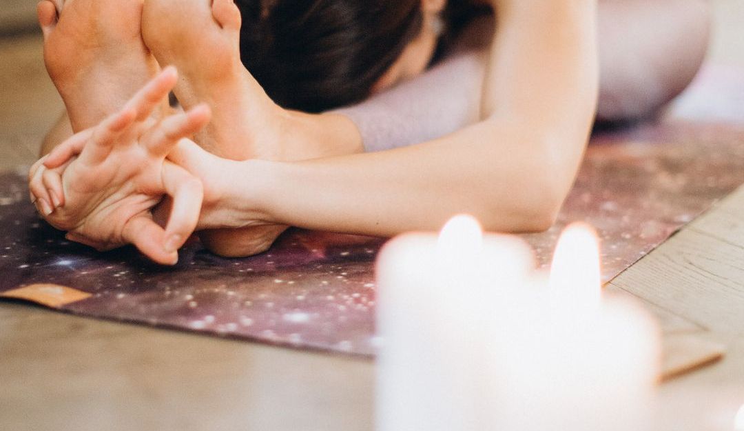 Person in einer Yoga-Pose auf einer Matte mit Kerzen im Vordergrund.