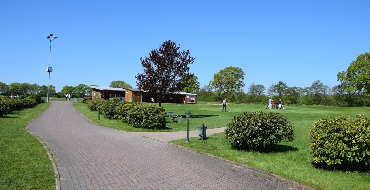 Golfplatz mit Übungsbereich und Personen beim Golfspielen unter blauem Himmel.