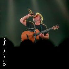 Ein Musiker auf der Bühne trinkt aus einer Flasche und hält eine Gitarre.