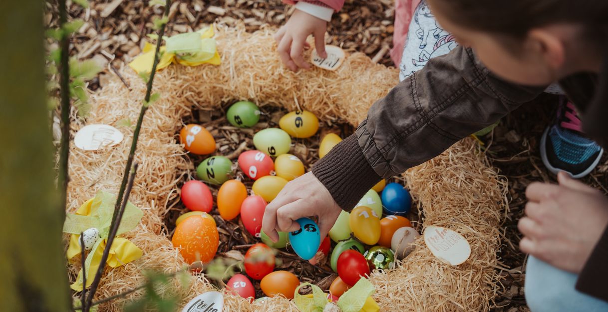 Kinder greifen nach bunten Ostereiern in einem Nest aus Stroh.