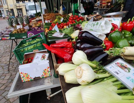 Ein Marktstand mit frischem Gemüse wie Paprika, Auberginen und Fenchel auf einem Wochenmarkt.