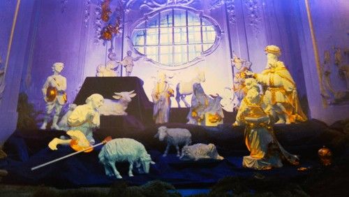 Krippenszene mit Figuren von Hirten, Schafen und Heiligen in einer Kirche.