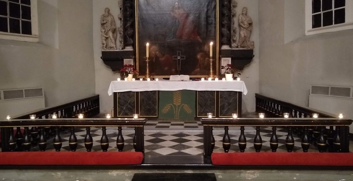 Ein Kirchenaltar mit Kerzen und Blumen geschmückt, flankiert von Statuen und einem Gemälde im Hintergrund.