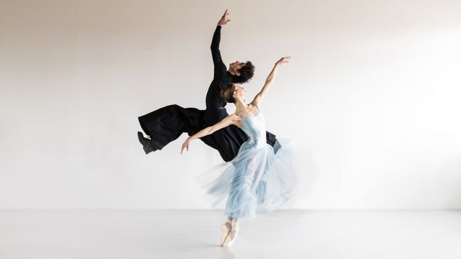 Zwei Balletttänzer in eleganten Posen in einem hellen Raum.