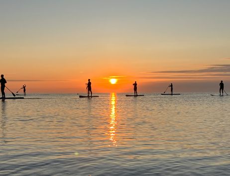 Personen beim Stand-Up-Paddling bei Sonnenaufgang auf dem Meer.