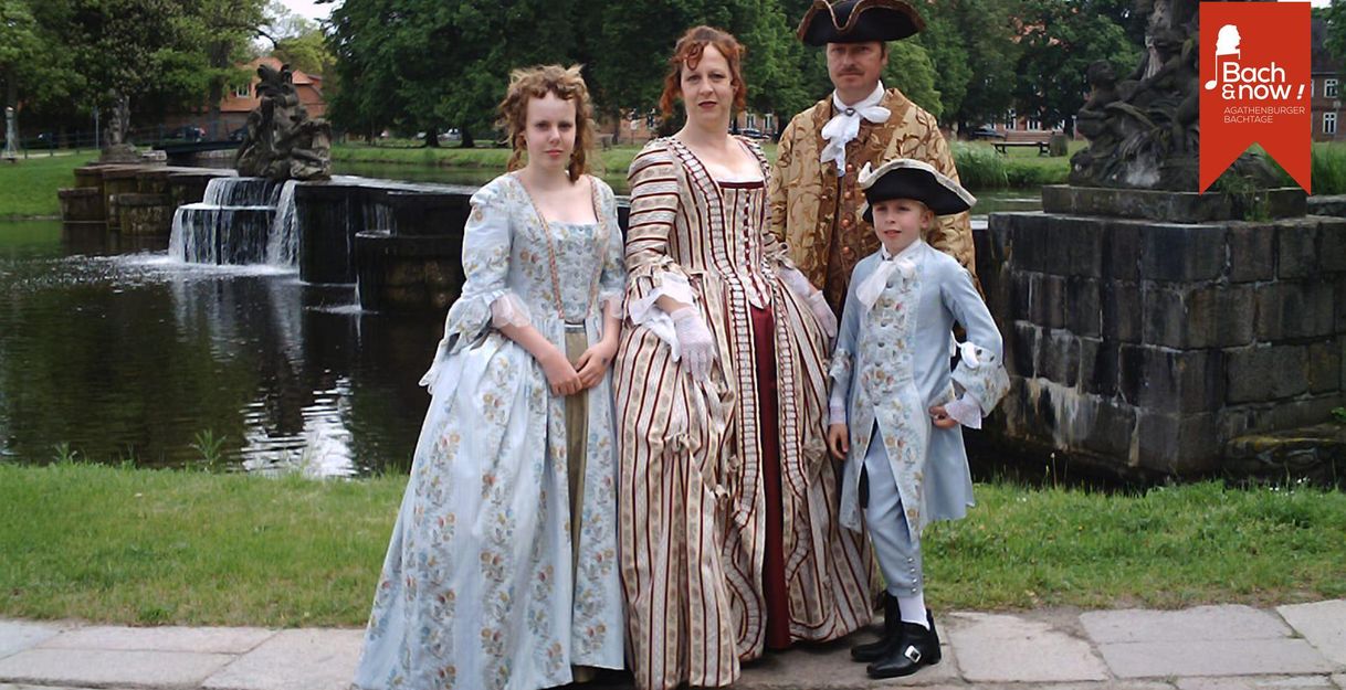 Eine Familie in historischen Kostümen steht vor einem Brunnen im Freien.